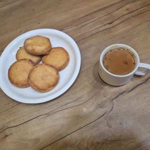 A white plate with freshly baked round cookies served next to a small cup of hot chai tea on a wooden table.